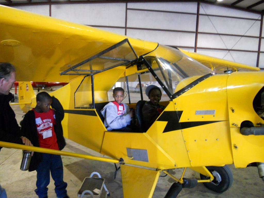 Children exploring the yellow aircraft cockpit in the hangar
